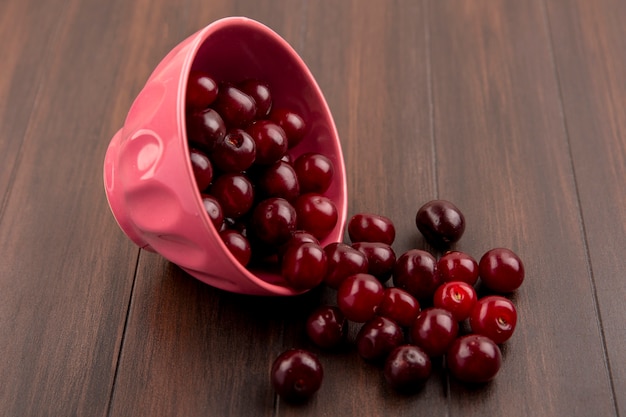 Side view of cherries spilling out of bowl on wooden background