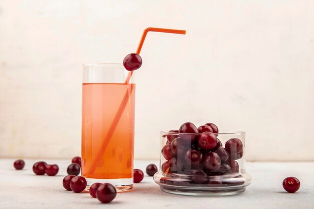 Side view of cherry juice with drinking tube in glass and cherries in jar and on white background