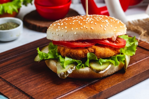 Side view chicken burger with sliced tomato and lettuce on the board