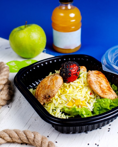 Side view of chicken cutlet with rice and tomato in a delivery box