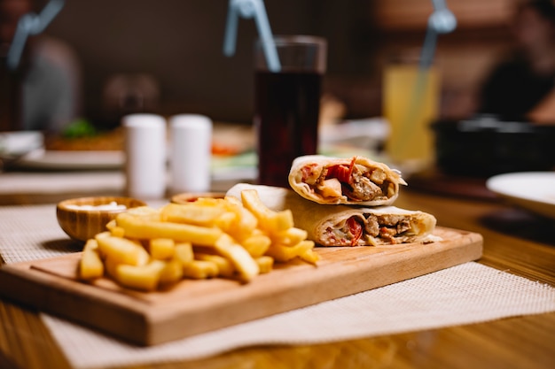 Вид сбоку куриный донер в лаваше с картофелем фри с кетчупом и майонезом на доске