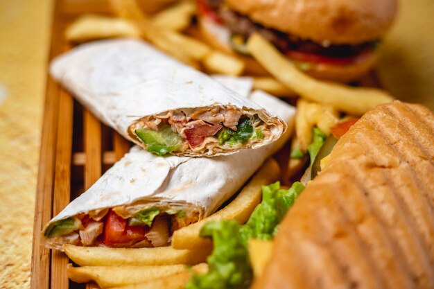 Side view chicken doner with tomato sauce cucumber in pita and french fries on the table Free Photo