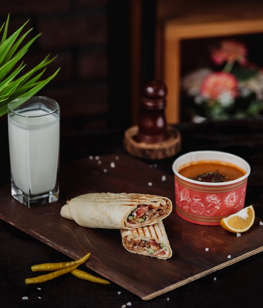 La vista laterale del doner di pollo avvolta nel lavash è servito con la zuppa di lenticchie merci e la bevanda di ayran su un bordo di legno
