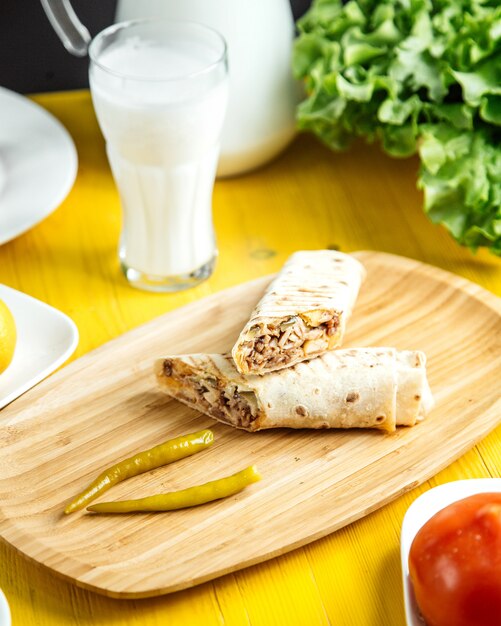 Side view of chicken doner wrapped in lavash with pickled green pepper on wooden platter