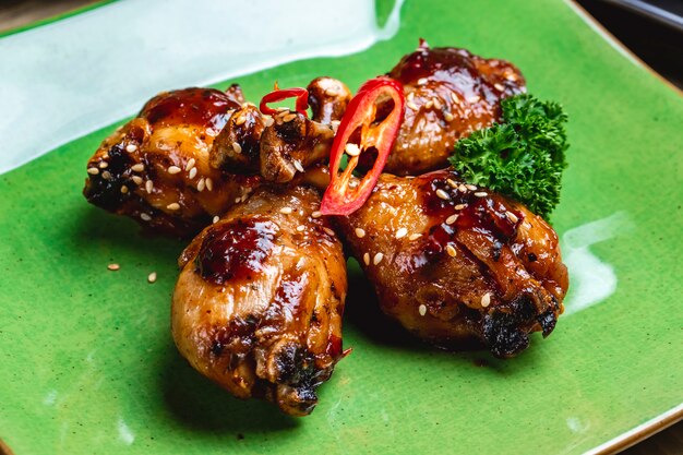 Side view chicken drumsticks fried chicken drumsticks in barbecue sauce wirh sesame seeds and bell pepper on a plate