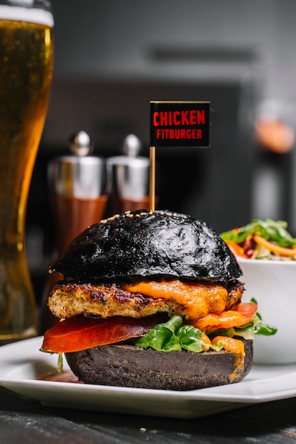 Foto gratuita fitburger di pollo vista laterale su un panino nero con un bicchiere di birra