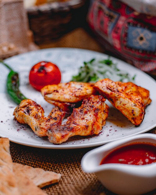 Side view of chicken kebab with grilled vegetables and spicy tomato sauce on the table