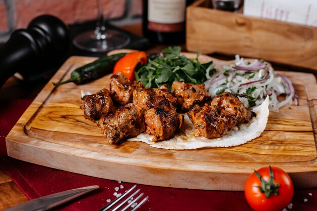 Side view of chicken kebab with onions and herbs on a wooden board