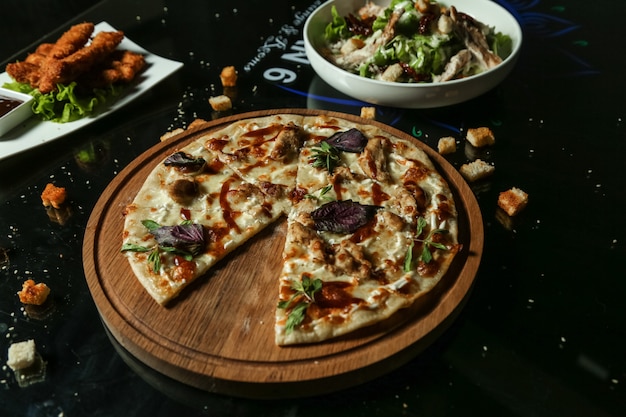 Вид сбоку куриная пицца на подносе с салатом на столе