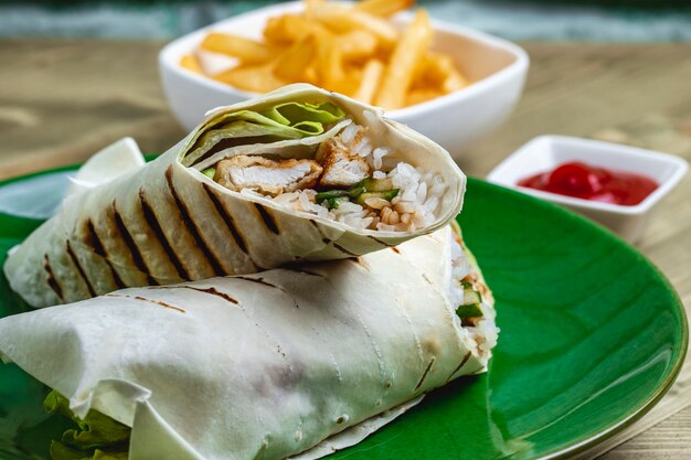 Side view chicken roll with lettuce leaf cucumber rice chicken strips ketchup and french fries on the table