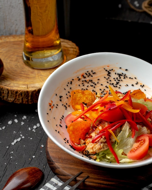 Side view of chicken salad with colorful bell peppers tomatoes potato chips and cumin seeds in a bowl on the table