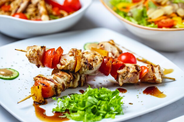 Side view chicken skewers grilled chicken with tomato bell pepper sauce and lettuce on a plate