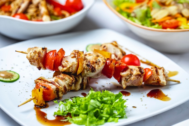 Side view chicken skewers grilled chicken with tomato bell pepper sauce and lettuce on a plate