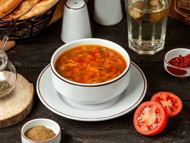 Side view of chicken soup with carrot and tomatoes in a white bowl