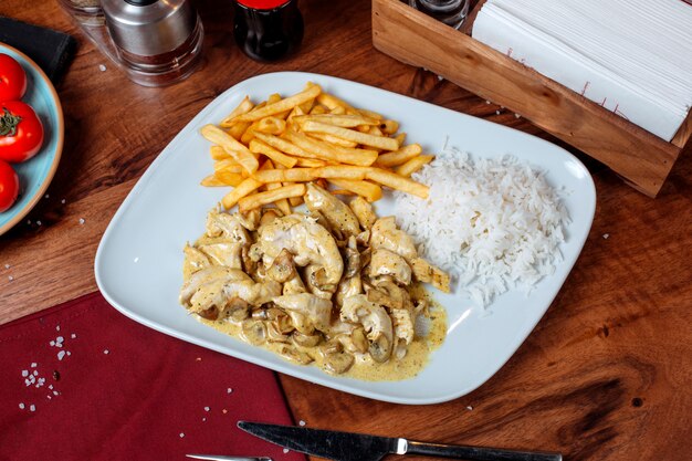 Side view of chicken stewed in a creamy sauce with mushrooms garnished with french fries on a white plate