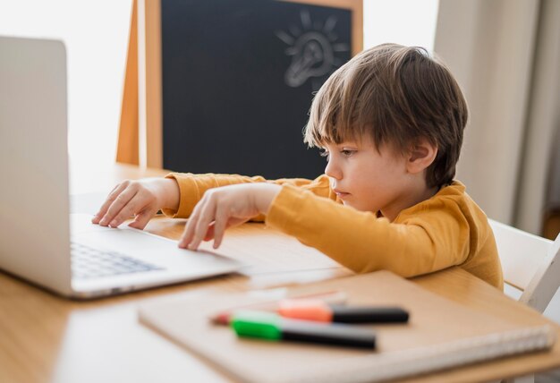 Вид сбоку ребенка за столом с ноутбуком и доской