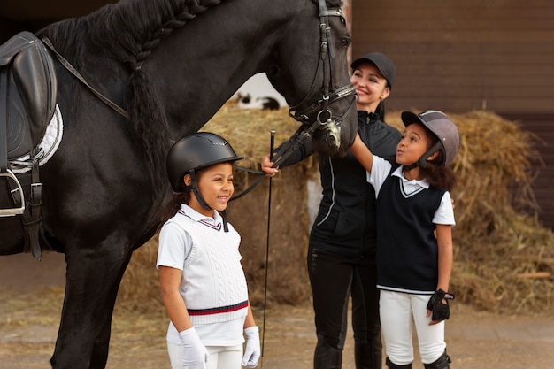 Free photo side view children learning to ride horses