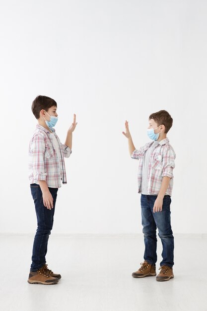 Side view of children with medical masks saluting each other