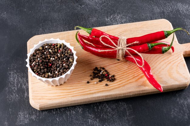Side view chili pepper with spices in white bowl on wooden cutting board on black stone
