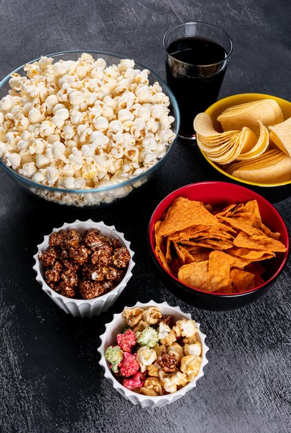 Side view of chips and popcorn in bowls on black vertical