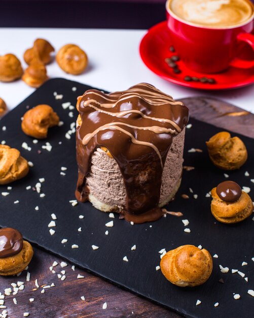 Side view of chocolate dessert decorated with profiteroles on a black wooden board