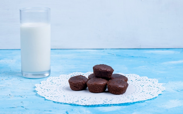 La vista laterale del muffin al cioccolato è servito con un bicchiere di latte sul blu