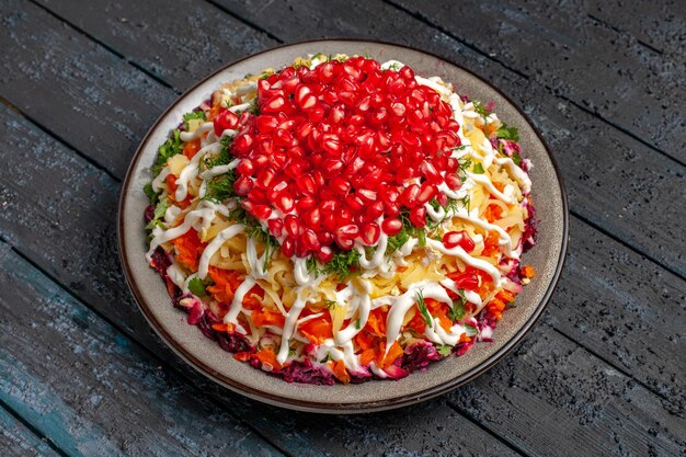 Side view Christmas food Christmas salad with potatoes carrots seeds of pomegranate and sauce in the plate on the grey table