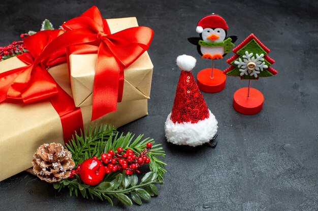 Side view of Christmas mood with beautiful gifts with bow-shaped ribbon and fir branches decoration accessories santa claus hat conifer cones on a dark background