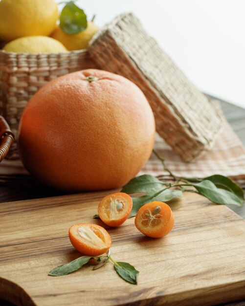 Side view of citrus fruits as kumquat slices with leaves on cutting board with orange and basket of lemon on wooden surface and white background