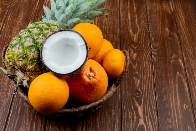 コピースペースを持つ木製の背景にバスケットにパイナップルココナッツオレンジタンジェリンとして柑橘系の果物の側面図