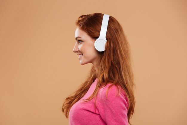 Side view close up portrait of a smiling redhead girl listening music with headphones
