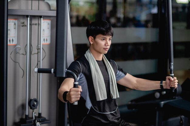 Side view, Close up Portrait Young handsome man in sportswear sitting for doing machine chest press exercise in modern gym, looking forward, 