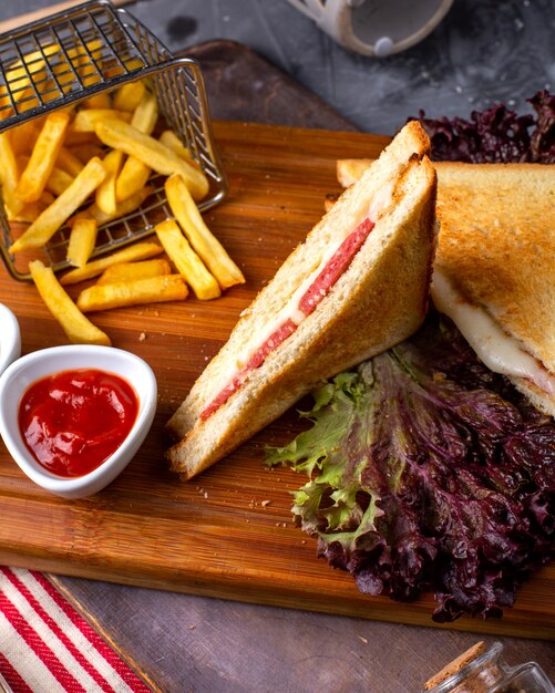 Side view of club sandwich with french fries and ketchup on wooden board