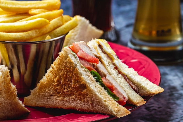 Боковой вид сэндвич с курицей-гриль, салатом из помидоров и картофелем фри на столе