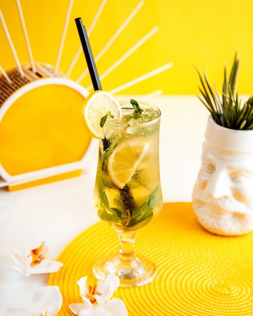 Side view of cocktail mojito with ice and lemon in a glass on yellow