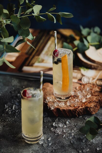 Side view of cocktails with ice and straw decorated with berries on a wooden stand