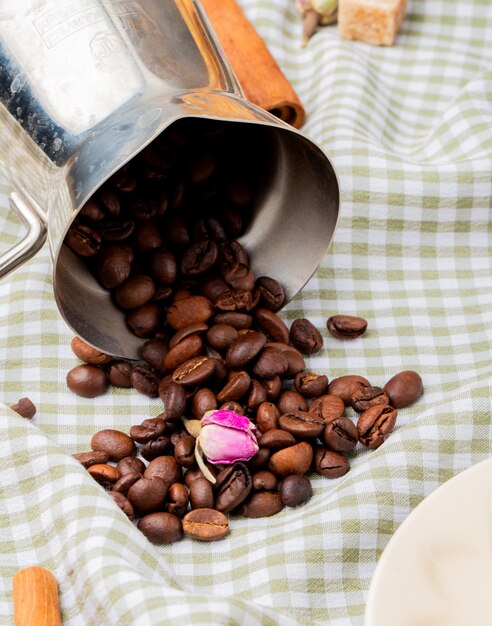 Side view of coffee beans scattered from a coffee pot on the plaid tablecloth