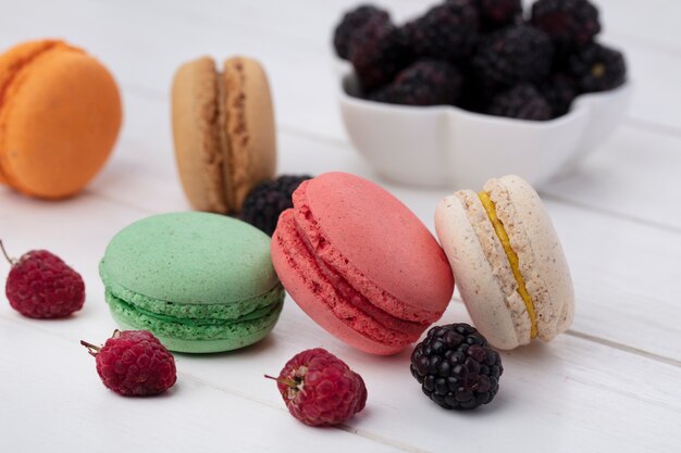 Side view of colored macarons with blackberries and raspberries on a white surface