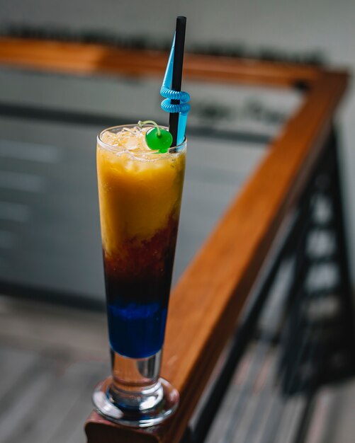 Side view of a colorful cocktail with ice and straw in a tall glass on dark background