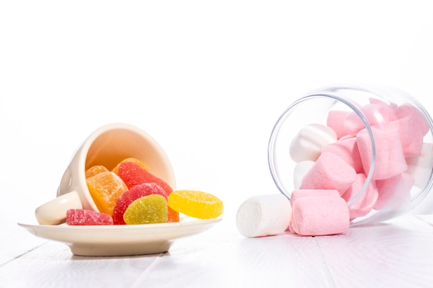Side view of colorful marmalade candies and marshmallow scattered on white