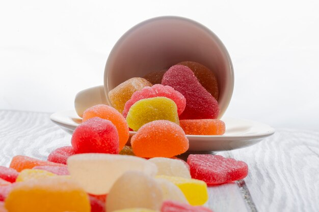 Side view of colorful marmalade candies scattered from a cup on white