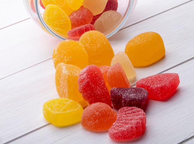 Side view of colorful marmalade candies scattered from a glass jar on rustic