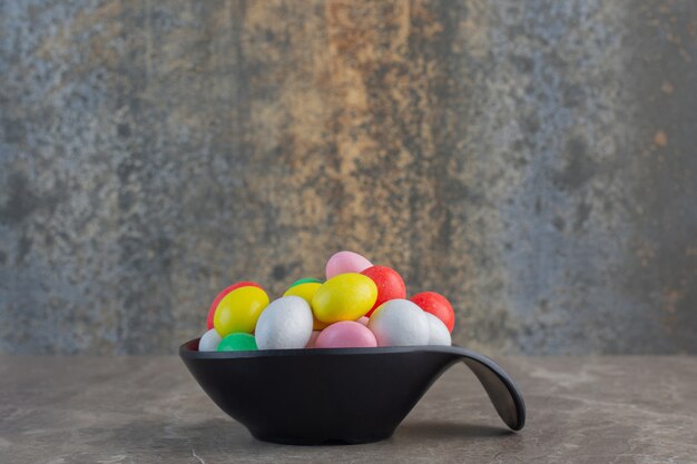 Вид сбоку красочных круглых конфет в черной миске на сером фоне.