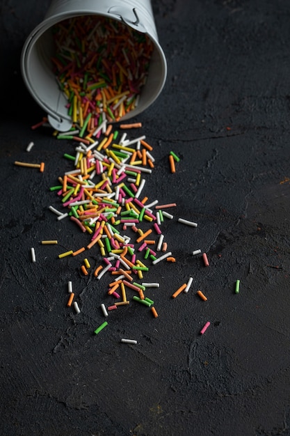 Side view of colorful sprinkles scattered from small bucket on black