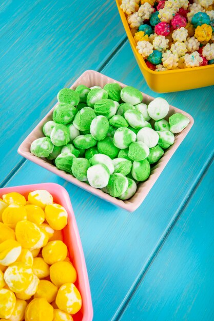 Side view of colorful sweet sugar candies in bowls on blue wooden background