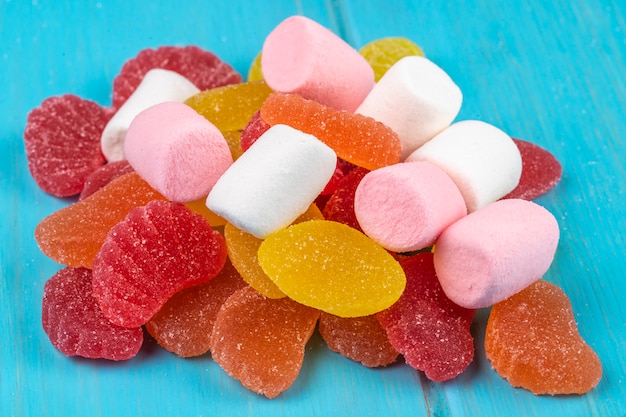 Вид сбоку красочные вкусные мармеладные конфеты и зефир, разбросанные на синем