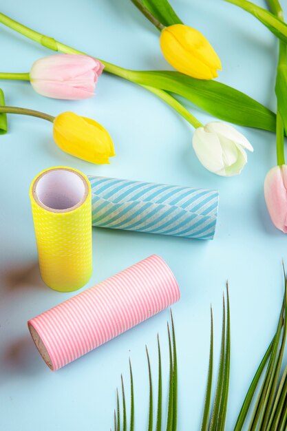 Side view of colorful tulip flowers and rolls of adhesive tape on blue background