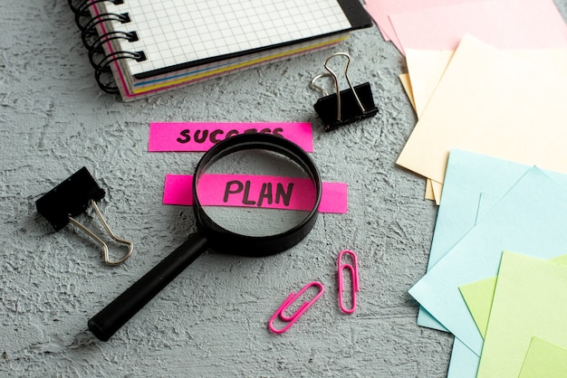 Free photo side view of coloured envelopes and success plan writings magnifying glass spiral notebook on gray sand background