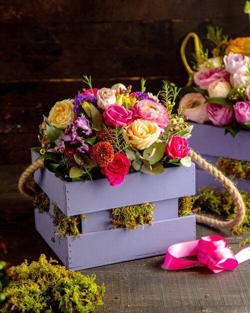 Вид сбоку композиции из розовых кустовых роз и цветов альстромерии с эвкалиптом в деревянной коробке