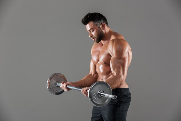 Side view of a concentrated strong shirtless male bodybuilder